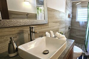 Un baño con un espejo grande, un lavamanos, una ducha y un inodoro.