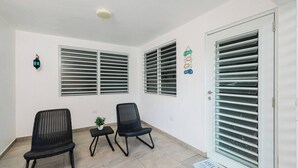 A room with two black wicker chairs, a small table with a plant, and a door with a window with horizontal blinds.