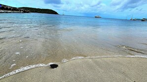 A beach with calm water, boats in the distance, and a rocky shoreline.