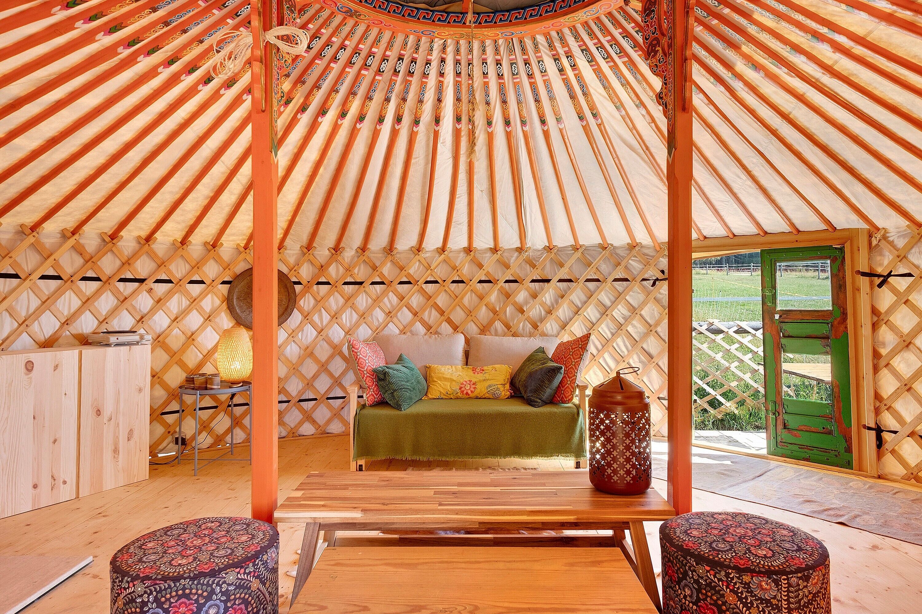 Interior de una yurtas con un banco de madera, un sofá con cojines, una mesa y un jarrón decorativo.