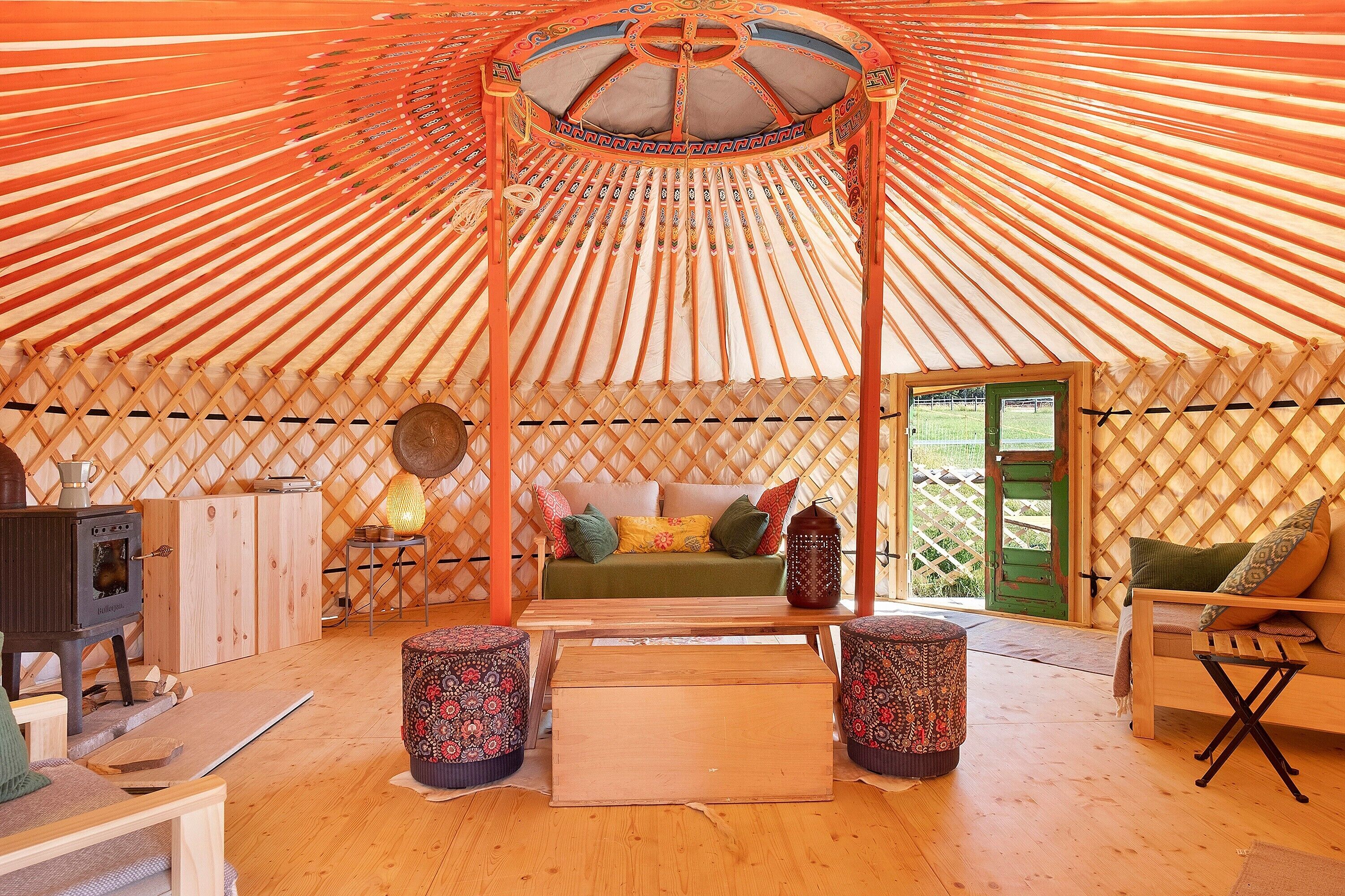 Interior de una yurta con suelo de madera, un sofá, una mesa y una estufa.