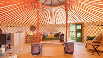 Interior de una yurta con suelo de madera, un sofá, una mesa y una estufa.