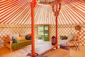 A yurt interior with a wooden bench, a sofa with cushions, a small table, and a decorative rug.
