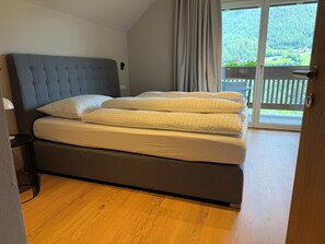 Ein Schlafzimmer mit einem Bett, einem Kopfteil, einem Fenster mit Vorhängen und Blick auf einen Balkon.