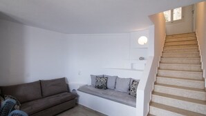 Un salon comprenant un canapé, un banc avec des coussins, un escalier et un luminaire fixé au mur.