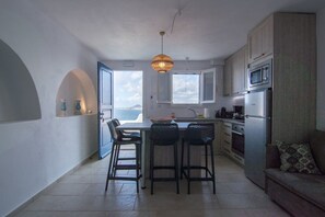 A modern kitchen with a central island, bar stools, a hanging light fixture, and a view of the sea through an open door. - Therys Maisonette, Divine Sea Views, Furnished Terrace, Semi Private Pool,. (Plaka)
