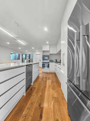 A modern kitchen with white cabinetry, stainless steel appliances, and a wooden floor. - Birkenhead Bliss | Serene 4Bed Home | Quiet, Views (Birkenhead)