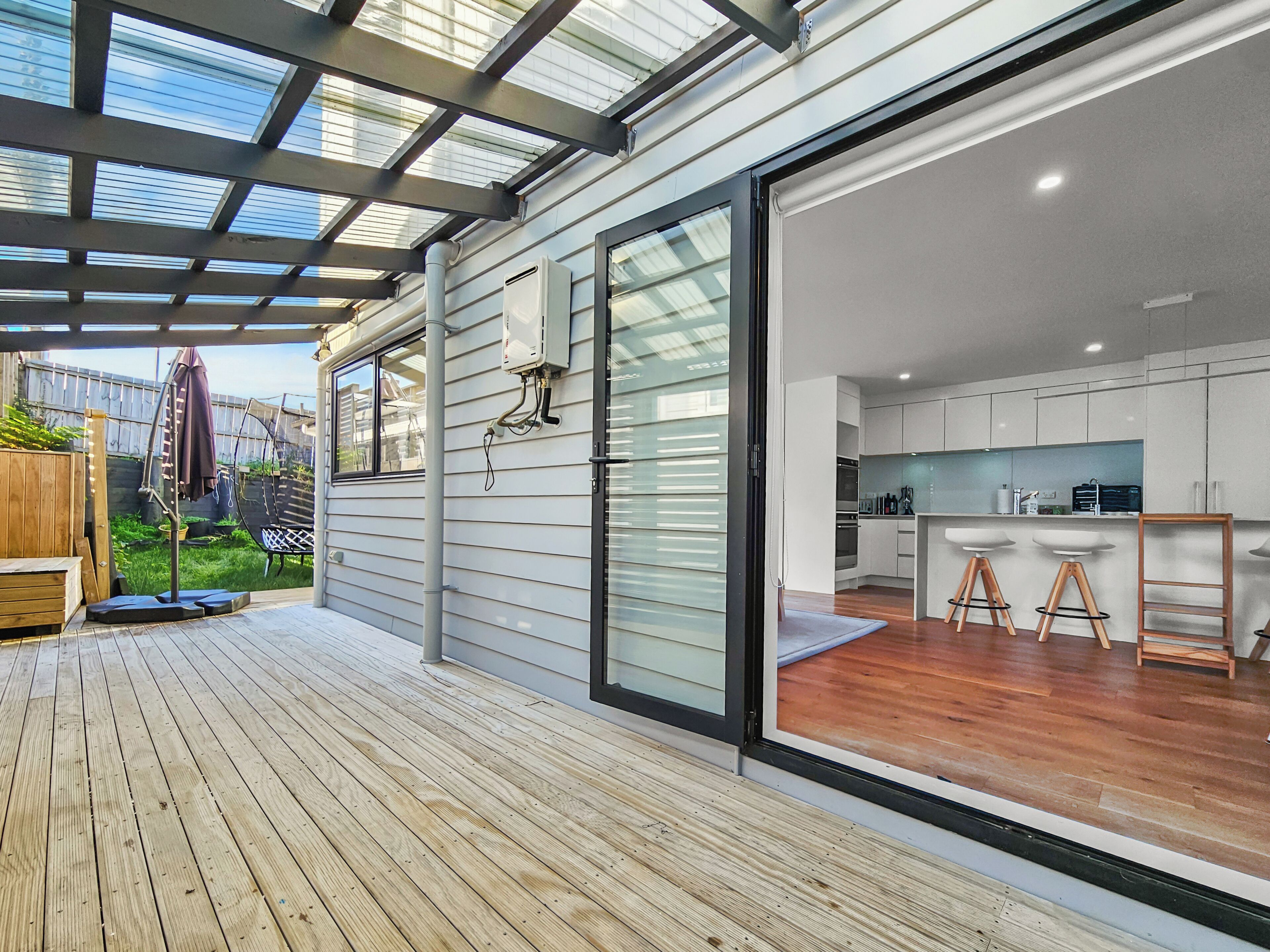 Une cuisine moderne avec des meubles blancs et un plancher en bois, donnant sur une terrasse dotée d’un toit en verre.