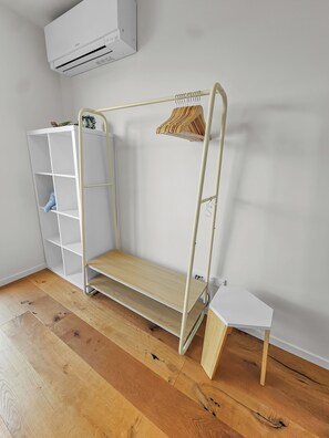 Ein Etagenbett mit Holzboden und einem weißen Nachttisch, eine weiße Regaleinheit und eine wandmontierte Klimaanlage.