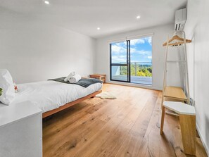 Ein Schlafzimmer mit einem Bett, Holzboden, einem großen Fenster und einem Kleiderständer.