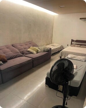 Ein Zimmer mit einer Couch, einem Bett und einem Standventilator.