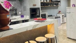 Et moderne køkken med en marmor bordplade, indbygget ovn og kaffemaskine. I baggrunden ses barborde og et køleskab.