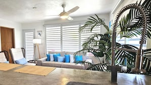 Ein Wohnzimmer mit einer Couch, einem Deckenventilator und einer großen Pflanze.