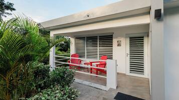 Um pátio moderno ao ar livre com guarda-corrimão branco, cadeiras vermelhas e uma porta com ripas horizontais.