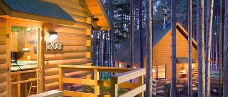Une cabane en rondins avec le numéro « 203 » sur la porte, une terrasse en bois et un paysage boisé en arrière-plan.