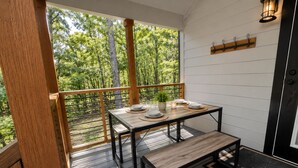 Um deck de madeira com mesa e banco, um vaso de planta, e vista para árvores.