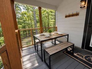 Eine Holzterrasse mit Tisch und Bank, einem Blumentopf und Blick auf Bäume.