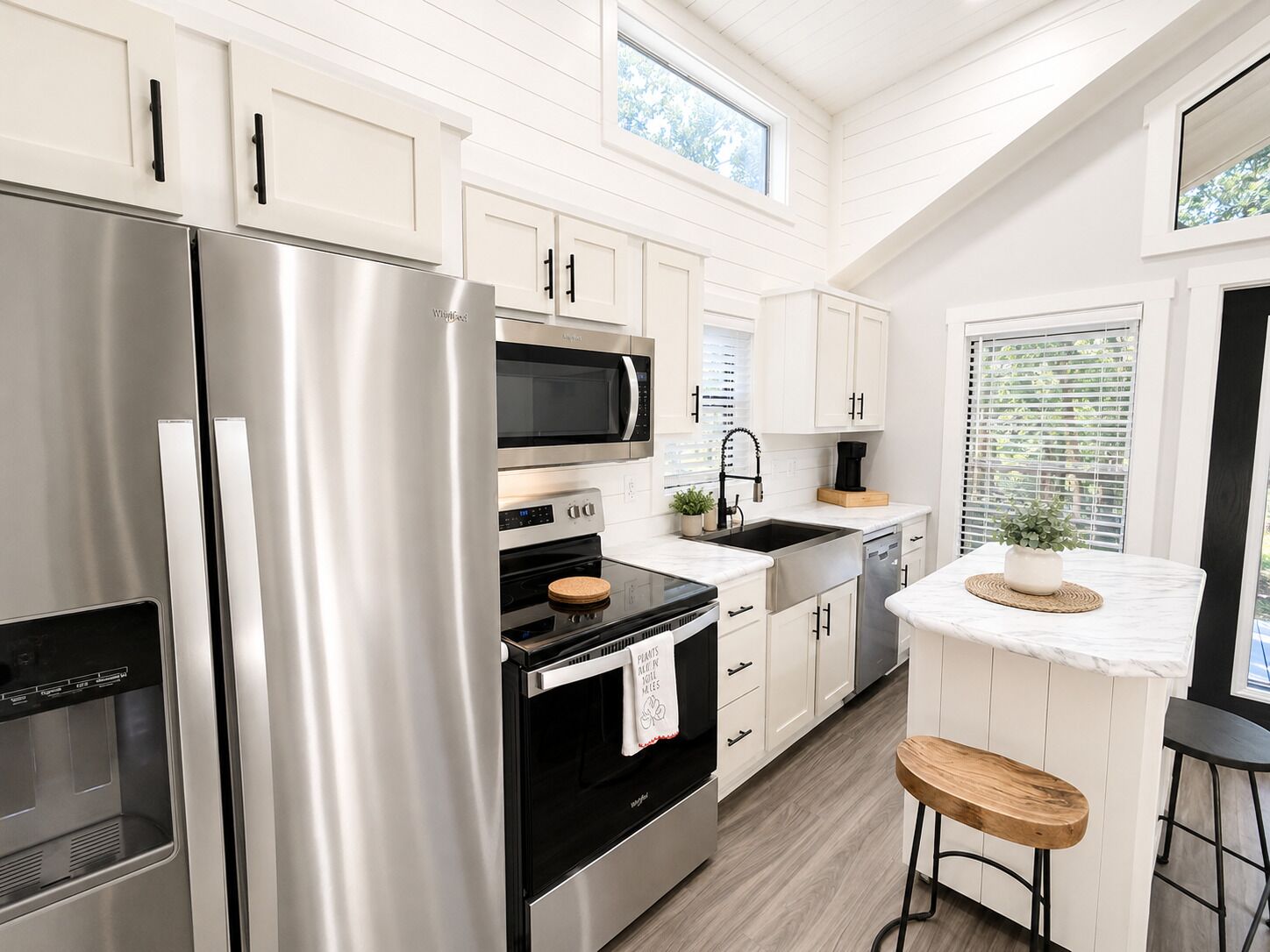 A modern kitchen with stainless steel appliances, white cabinetry, and a wooden bar stool.