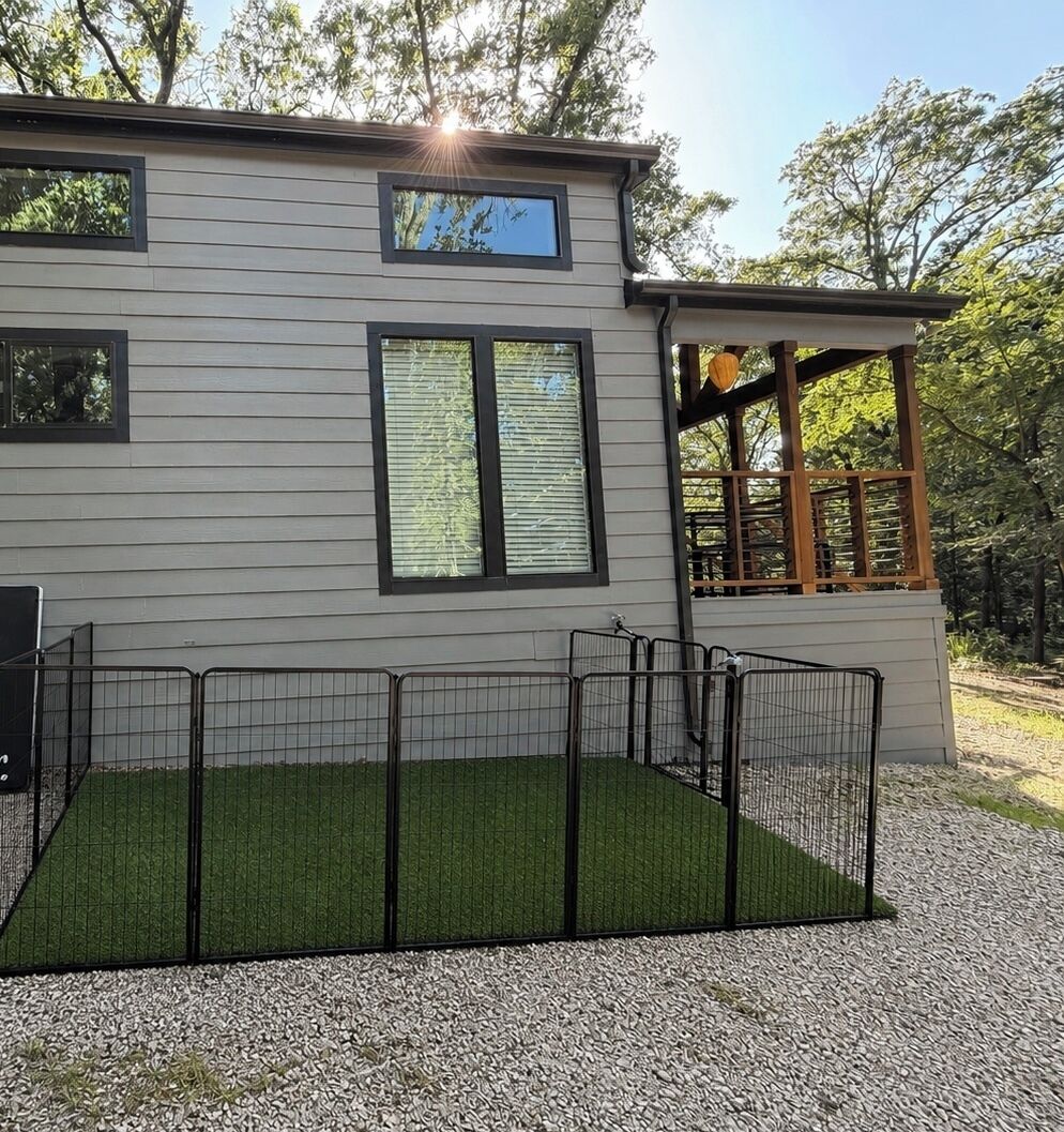 A modern two-story house with a fenced outdoor area featuring artificial grass.