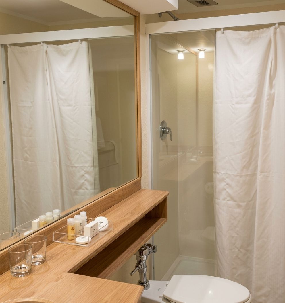Une salle de bain avec une douche à parois de verre, un meuble-lavabo en bois avec un miroir et des toilettes blanches.