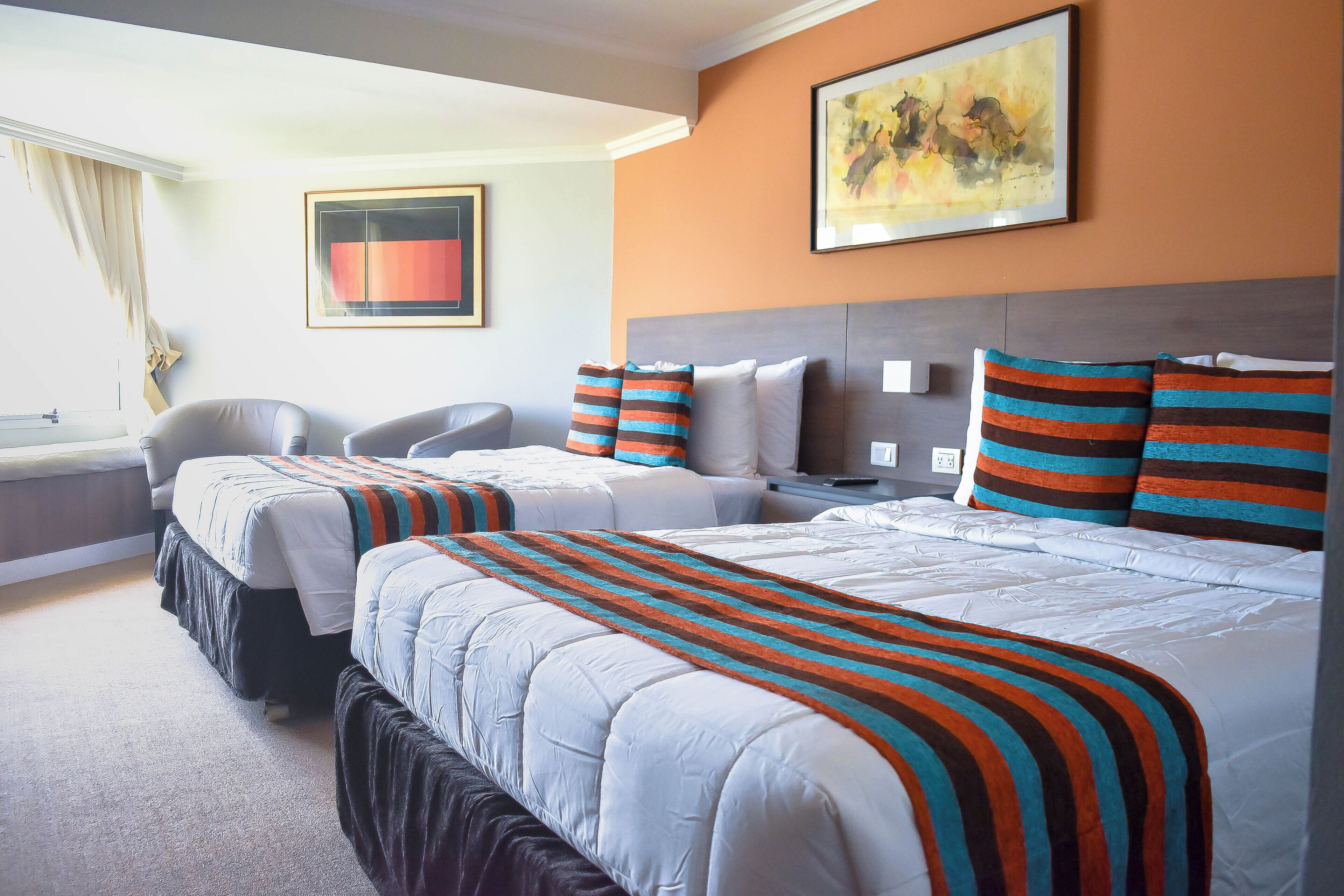 A hotel room with two beds, a desk, a chair, and a painting on the wall.