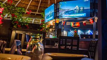 A restaurant interior with a thatched roof, multiple screens displaying sports content, and a variety of flags.