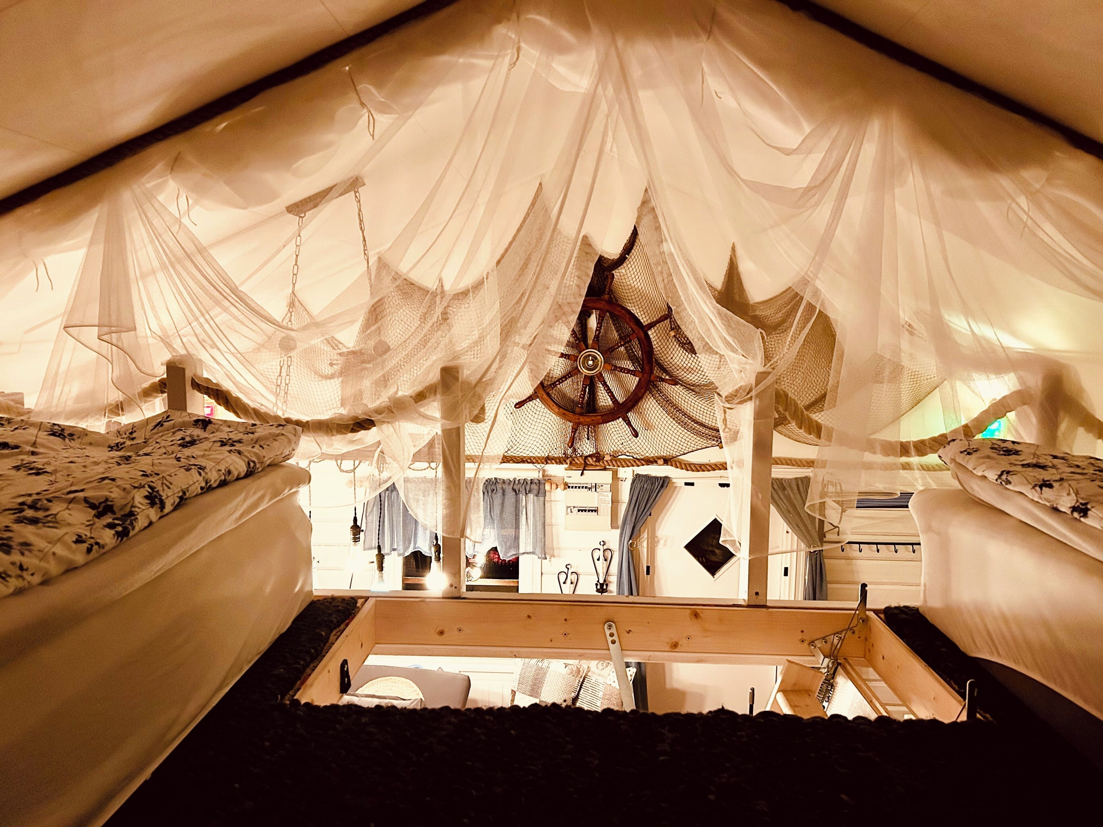 A tent-like room with a bed, a wooden ladder, and a wheel-like structure.