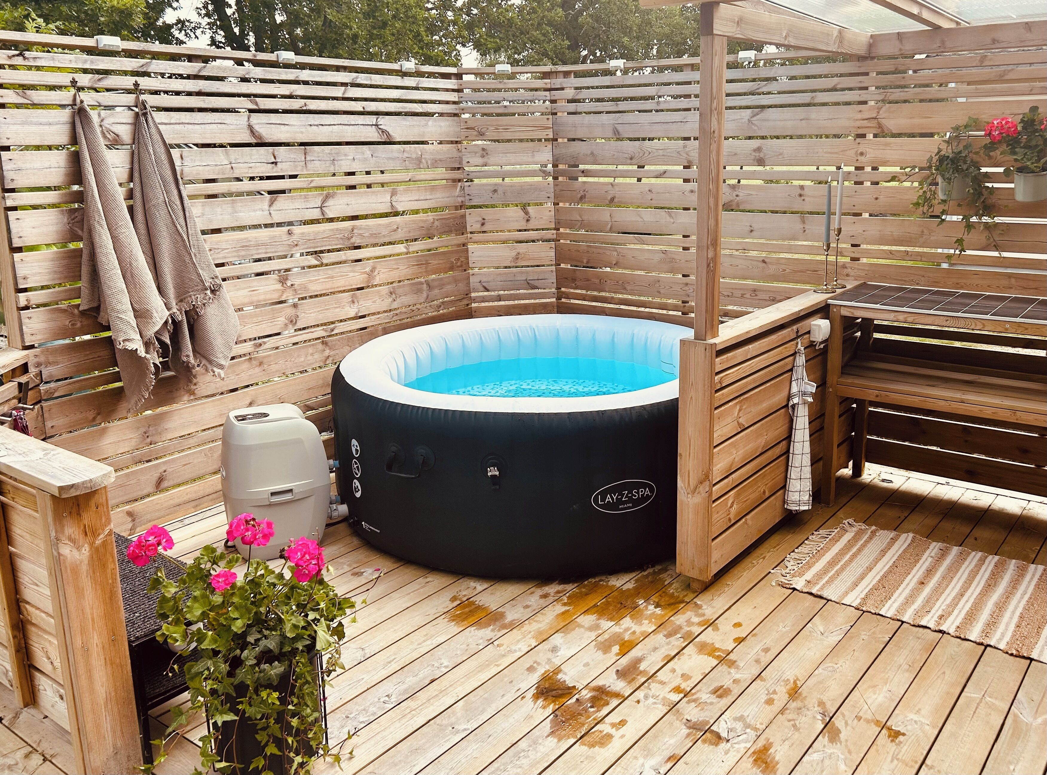 Eine Holzterrasse mit Whirlpool, Grill und einer Holzpergola.