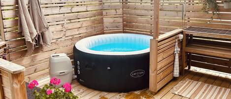 Eine Holzterrasse mit Whirlpool, Grill und einer Holzpergola.