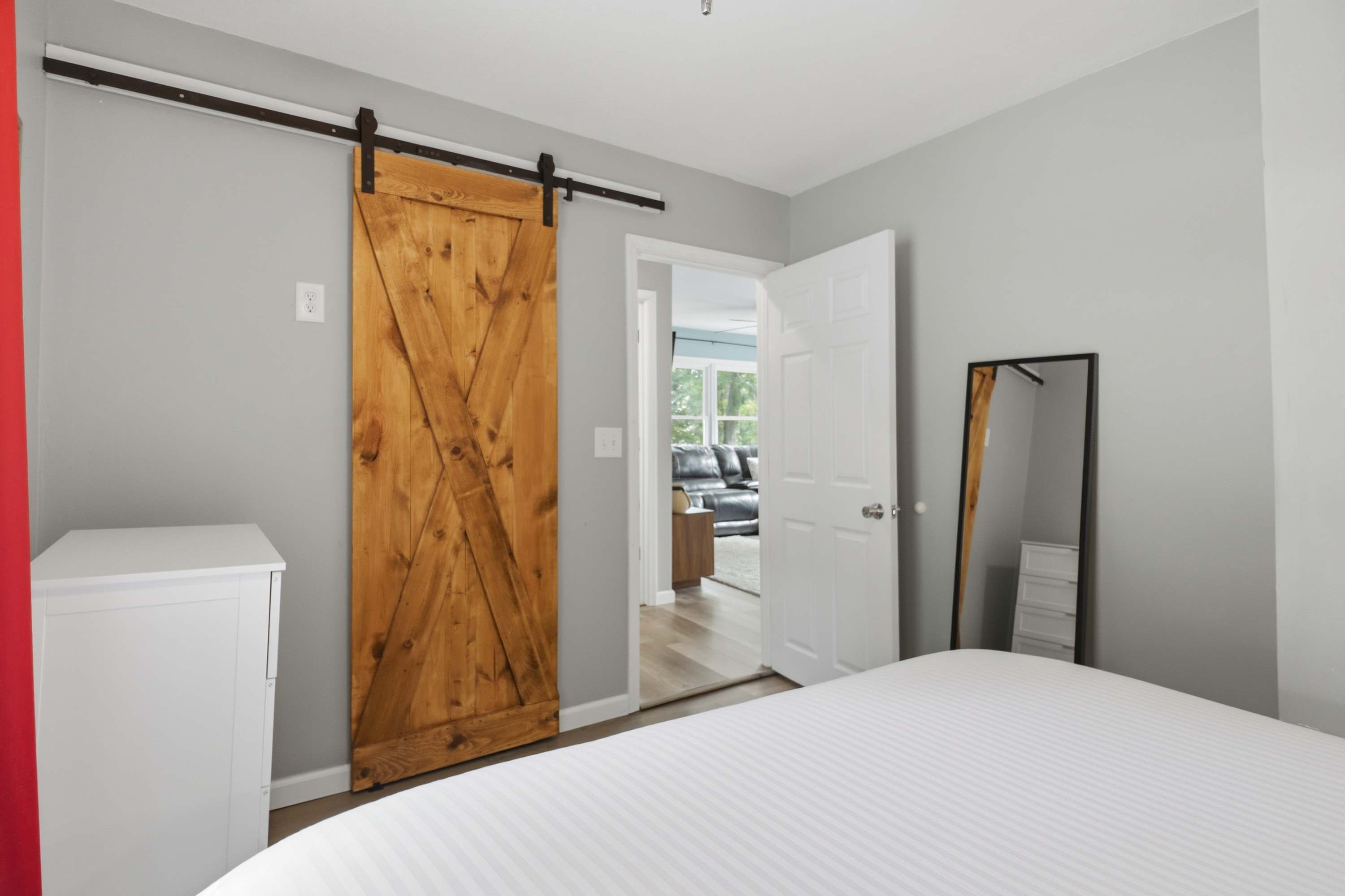 Un dormitorio con cama, armario, espejo y puerta que da a otra habitación.