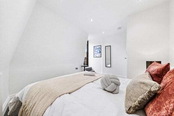 A modern bedroom with a large bed, a bedside table, and a wall-mounted mirror.