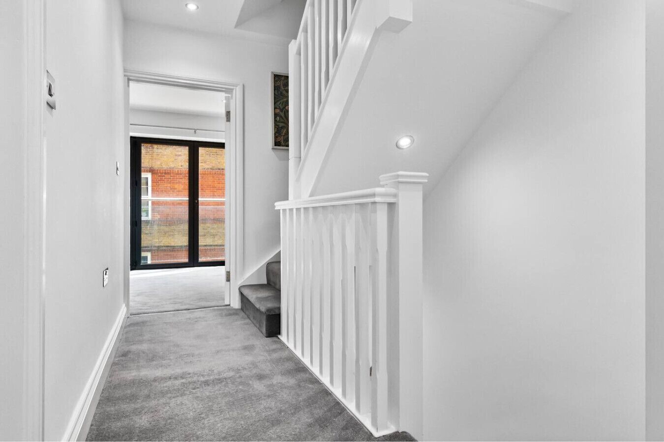 A hallway with a carpeted floor, white walls, a white railing, and a door leading to a brick exterior.