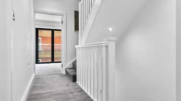 A hallway with a carpeted floor, white walls, a white railing, and a door leading to a brick exterior.