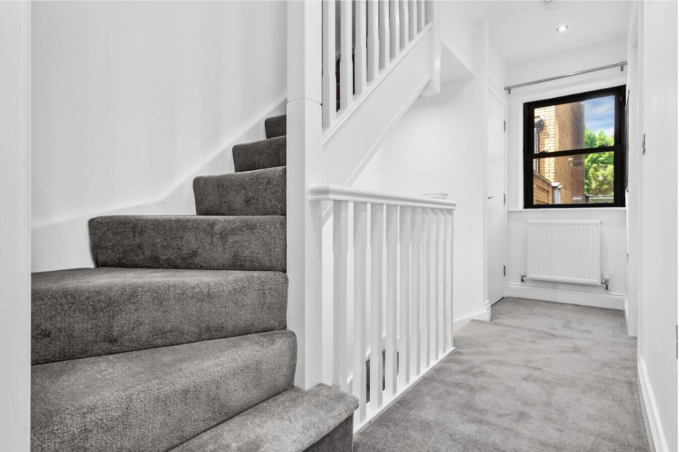 Eine Treppe mit weißen Geländern, mit Teppich belegten Stufen und Blick durch ein Fenster nach draußen.