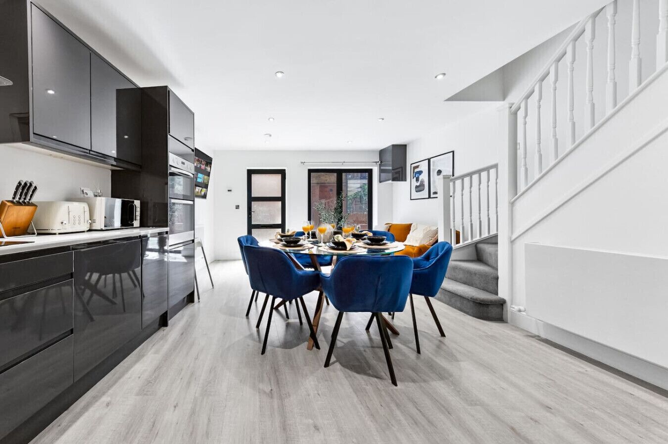 Une cuisine moderne avec des meubles de couleur sombre, un coin repas avec des chaises bleues et un escalier.