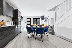 A modern kitchen with dark cabinets, a dining area with blue chairs, and a staircase.