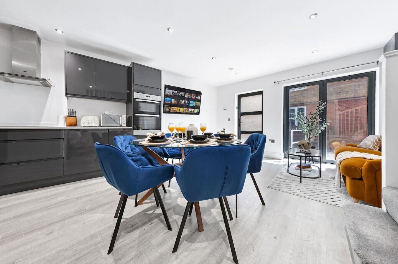 A modern kitchen with dark cabinets, a dining area with blue chairs, and a sofa with a cushion.