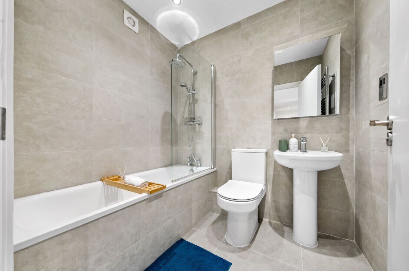 A modern bathroom with a glass-enclosed shower, a white bathtub, a white toilet, and a pedestal sink.