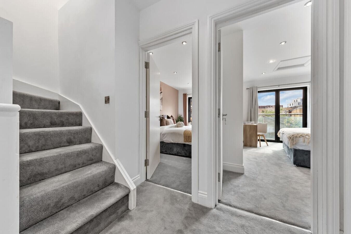 A staircase leading to a bedroom with a large window, a balcony, and a view of buildings.