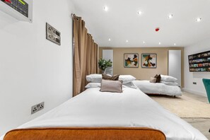 A hotel room with two beds, a large window with curtains, a plant, artwork on the walls, and a bookshelf. - Luxurious 5 BED | Sleeps 14 | Tower Bridge (Greater London)