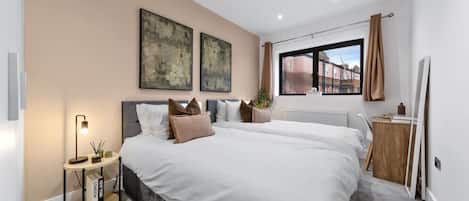 A modern bedroom with a large bed, bedside tables, a desk, and a window with curtains.