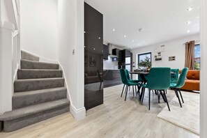 A modern interior with a staircase, a dining area with teal chairs, and a kitchen in the background. - Luxurious 5 BED | Sleeps 14 | Tower Bridge (Greater London)
