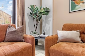 Ein modernes Wohnzimmer mit zwei braunen Ledersofas, einem Blumentopf, einem kleinen Tisch mit Büchern und einem Bild an der Wand.