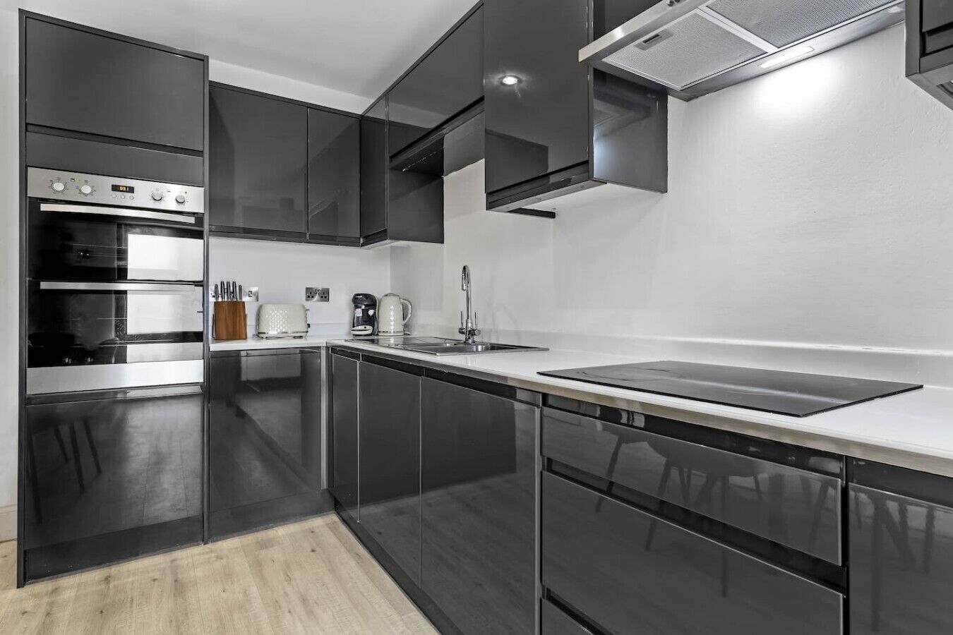 A modern kitchen with dark cabinetry, a stainless steel range, a built-in oven, a coffee maker, and a sink.