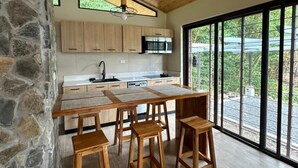 A modern kitchen with wooden cabinets, a large island, and a dining area with wooden stools. - Mountain View Fully Equipped Villa (El Valle de Antón)