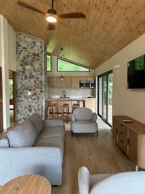 A modern interior with a stone accent wall, a kitchen with wooden cabinets, a dining area, and a seating area with sofas and a TV. - Mountain View Fully Equipped Villa (El Valle de Antón)