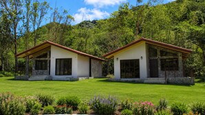 Two small, single-story buildings with stone foundations and red roofs, surrounded by a well-maintained lawn and flowering plants. - Mountain View Fully Equipped Villa (El Valle de Antón)