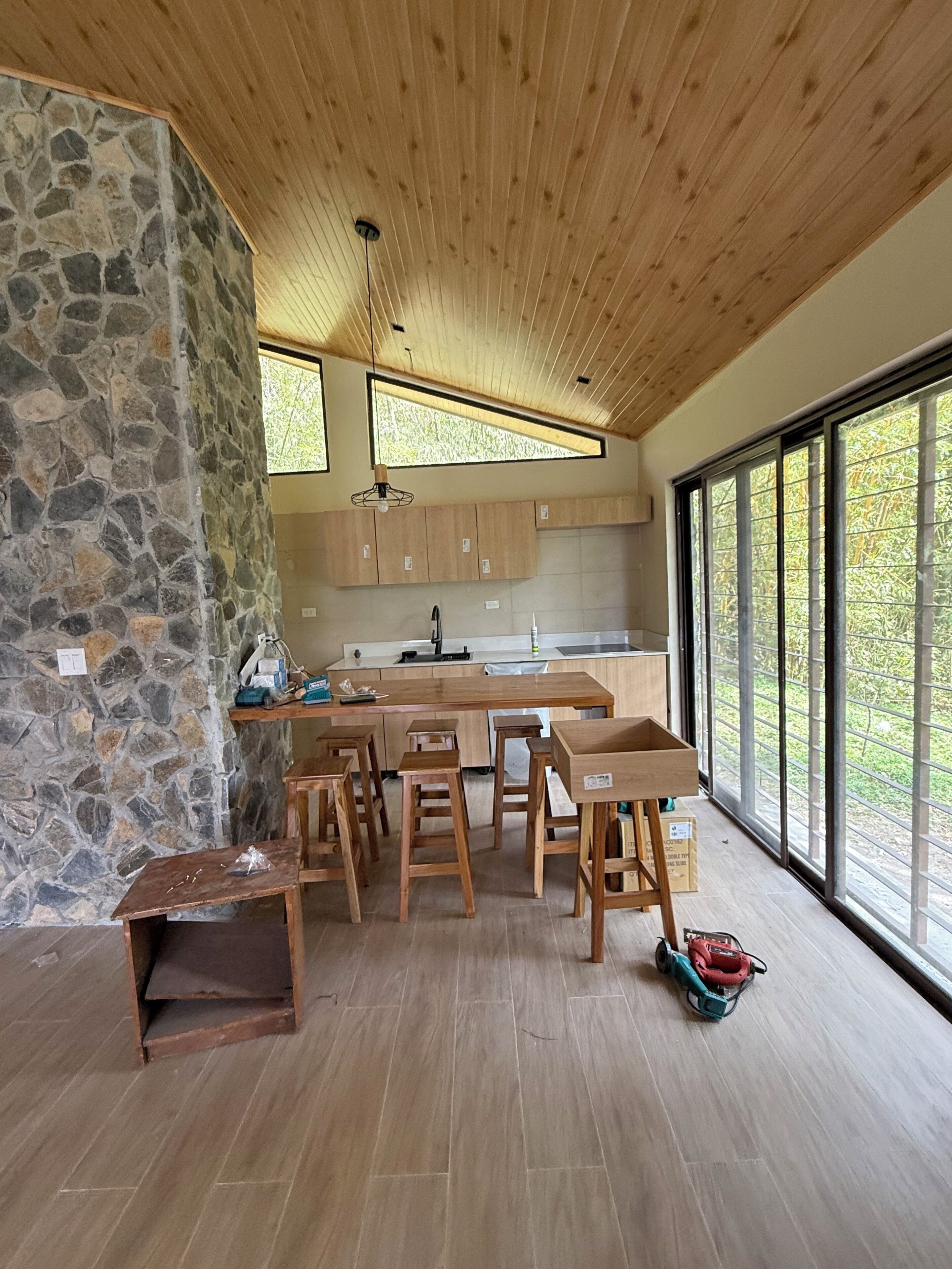 A modern kitchen with a stone wall, wooden ceiling, and large windows.