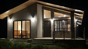 A modern house with a large sliding glass door, a staircase leading to the entrance, and a well-lit exterior.