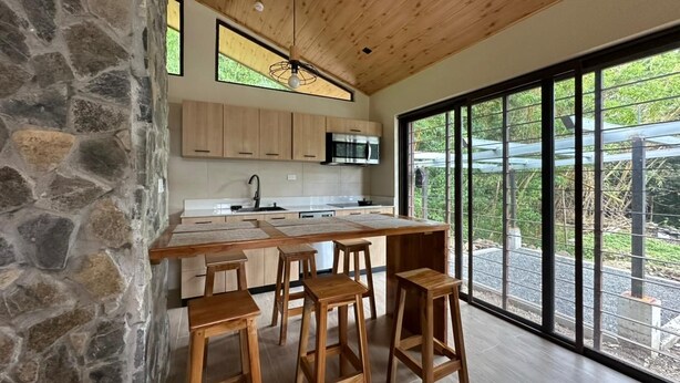 A modern kitchen with a stone wall, wooden ceiling, and large windows. - Mountain View Fully Equipped Villa (El Valle de Antón)